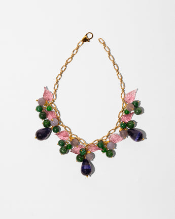A gold-tone chain necklace with pink and green floral embellishments, featuring faceted green beads, pink enamel leaves, and teardrop-shaped purple and green stones, displayed on a clean white background.