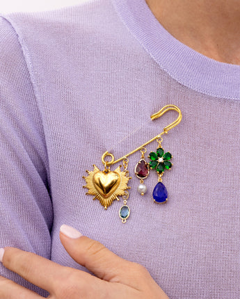 a close up of the Katerina Psoma Amulet brooch — sunburst gold heart, crystal flower and crystal drop charms with a pearl accent, on a gold safety pin