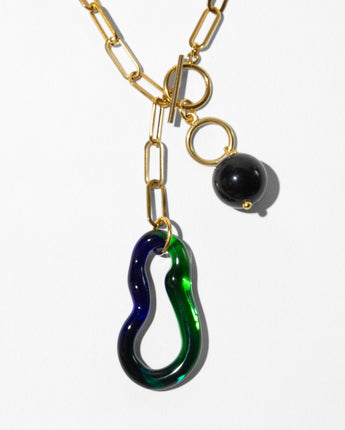 a close up of Katerina Psoma Plume necklace — Murano glass wave pendant and blue goldstone bead on a gold paperclip chain