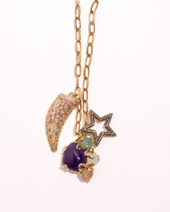Close up detail of Katerina Psoma Selene necklace — crystal horn, amethyst stone cluster and blue crystal star charms on a long gold chain