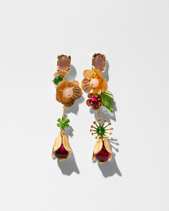 A pair of ornate gold dangle earrings with floral and botanical details, featuring peach cabochons, amber petals, green enamel leaves, and deep red teardrop pendants, set against a clean white background.