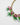 A close-up of a statement necklace featuring pink floral clusters with green stem details, white pearl-like beads, and a gold chain on a light gray background.