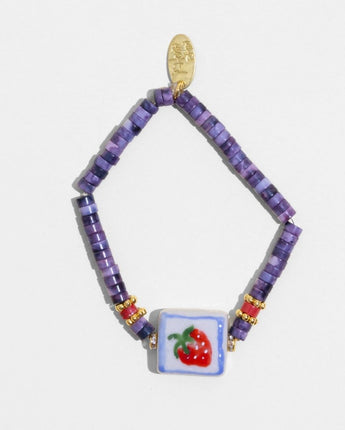 Bracelet with purple beads and a strawberry charm on a white background