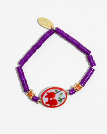 Bracelet with purple beads and a decorative red and white charm on a white background
